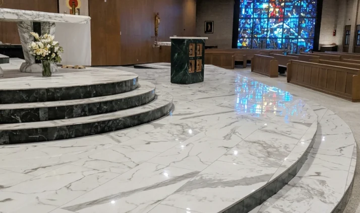 Escadarias curvas em pedra natural e piso claro em igreja com vitrais coloridos.